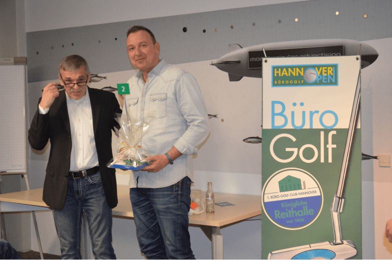 Andreas Stein, Geschäftsführer der steindesign Werbeagentur und Gründer des 1. Büro-Golf-Club Hannover übergibt den 2. Preis an Falco Schleier. Dieser erhält ein metallisches Bürogolfloch mit Klappmechanismus.