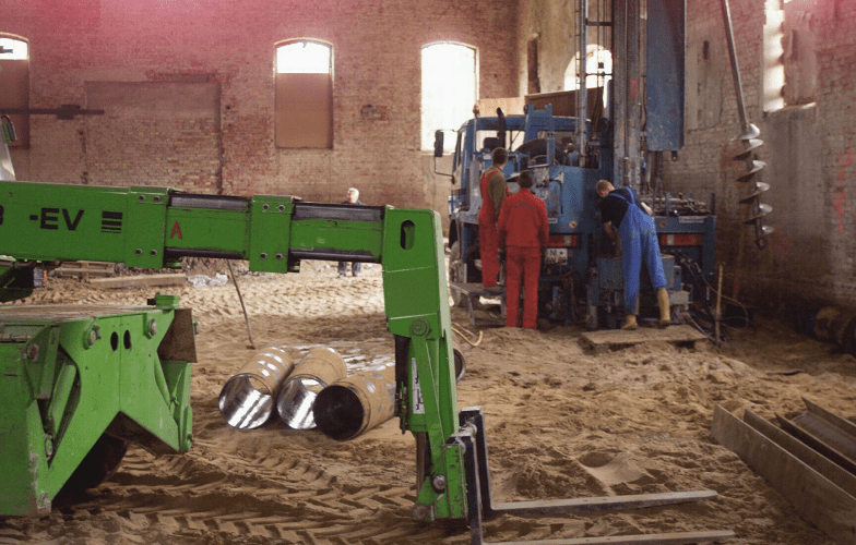 Zu sehen sind Bauarbeiten auf sandigem Boden zur Stabilisierung der alten Reithalle, da diese ursprünglich kein Fundament besaß, sondern flach auf dem Boden stand.