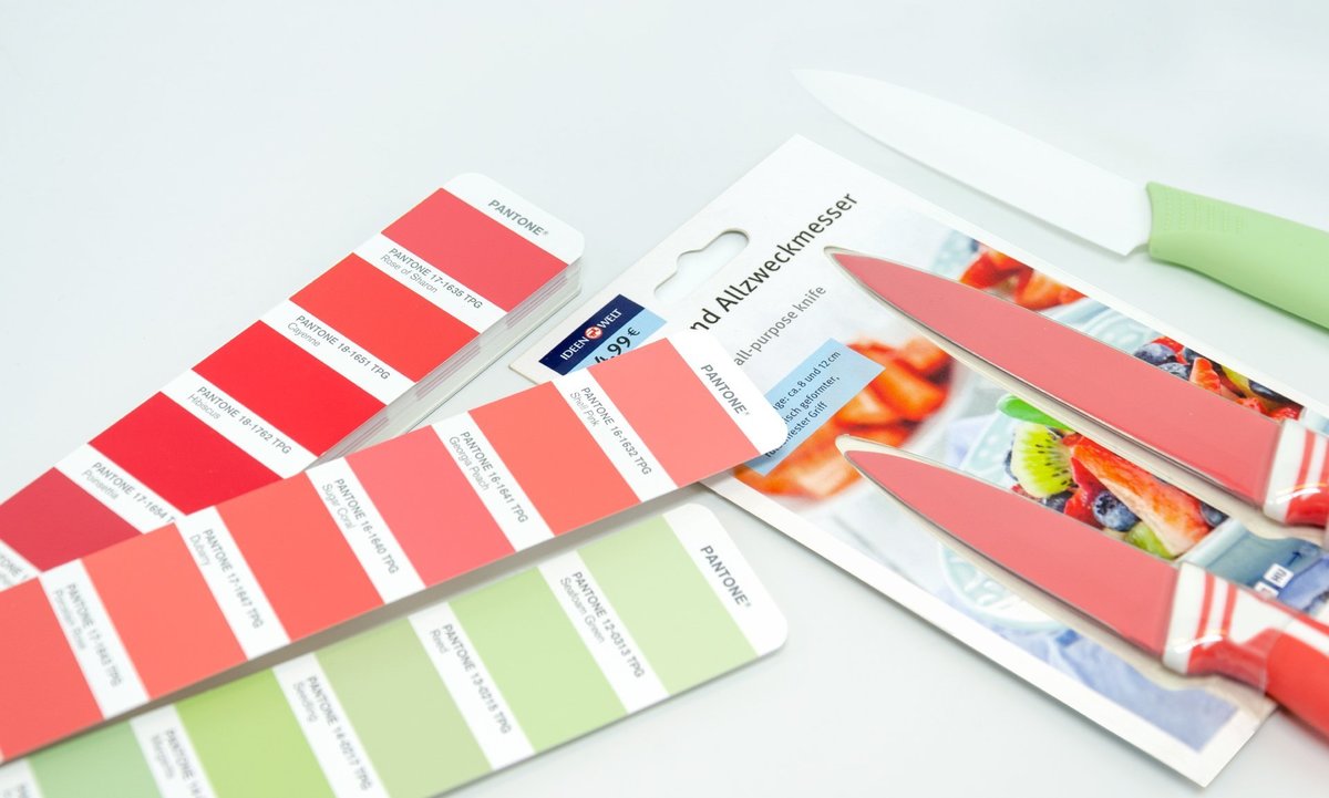 Das Foto zeigt die Verpackung von verschiedenfarbigen Allzweckmessern für die Rossmann Ideenwelt. Links daneben liegen Farbkarten aus einem Pantone-Fächer mit den vorgegebenen Tönen.