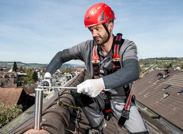 Das Foto ist ein Titelbild der TIPPS, das einen Arbeiter mit Persönlicher Schutzausrüstung gegen Absturz zeigt, der am Dachfirst eine Sicherung installiert.