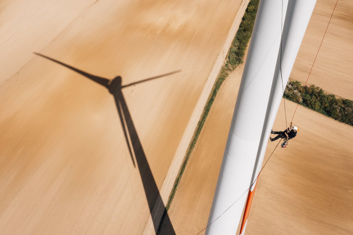 Das Bild zeigt die Rotorblattinspektion einer Windenergieanlage per Abseiltechnik in großer Höhe. Es sieht aus, als würde der Inspekteur am Rotorblatt hinauflaufen.